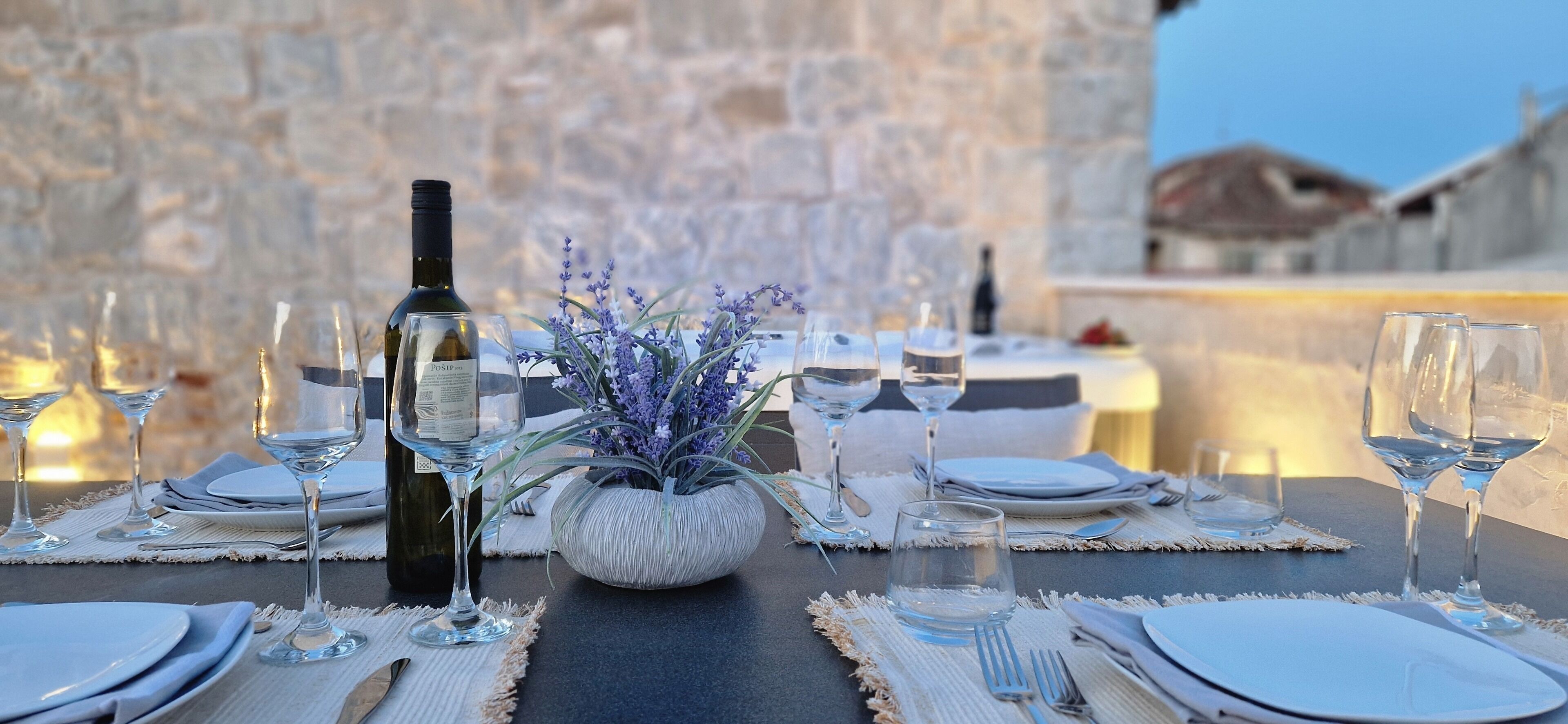 Una tavola imbandita per un pasto, con calici di vino, piatti e un vaso di fiori.