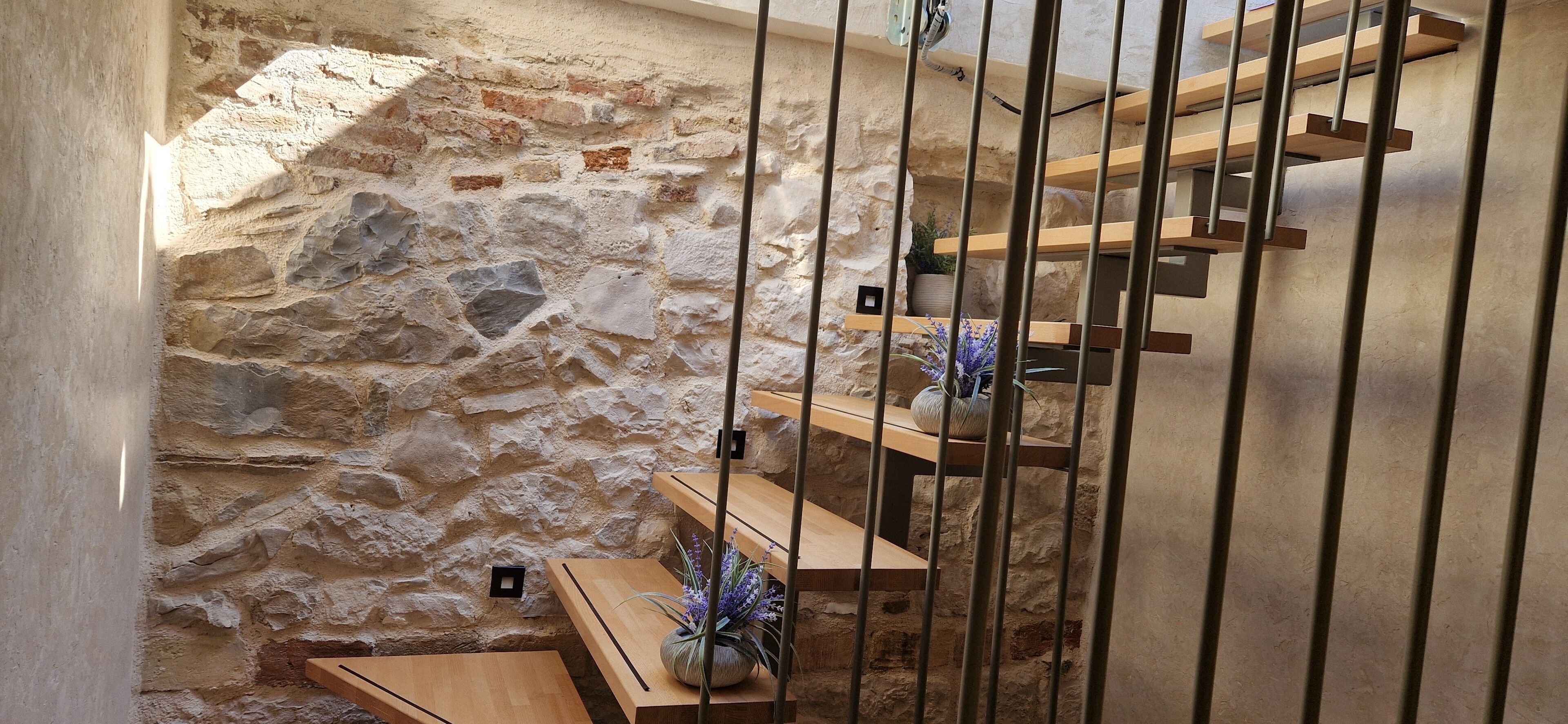 A stone-walled interior with a wooden staircase and a metal railing.