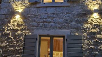 Un edificio de piedra con múltiples ventanas, algunas con contraventanas, e iluminación exterior.