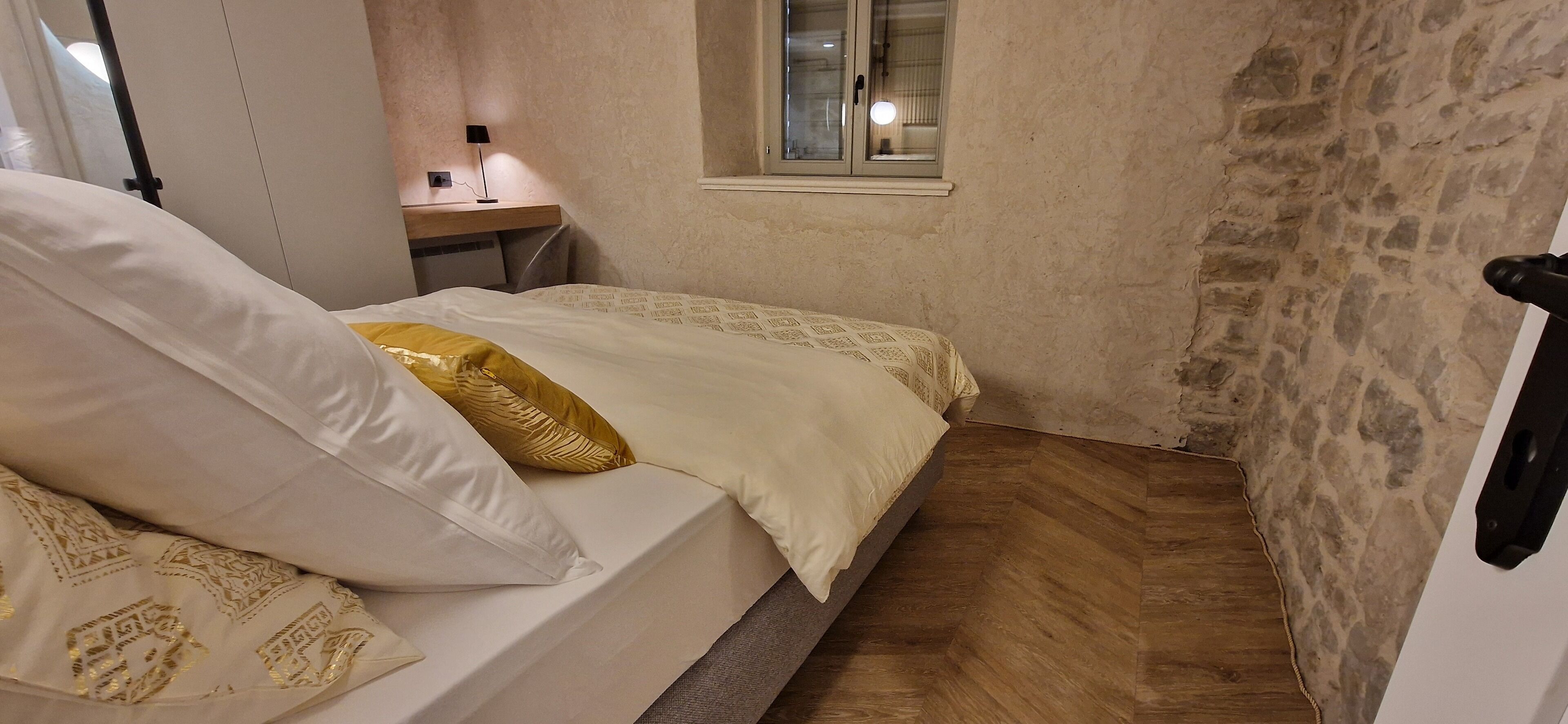 Een kleine, gezellige slaapkamer met een bed, nachtkastje, lamp en raam.