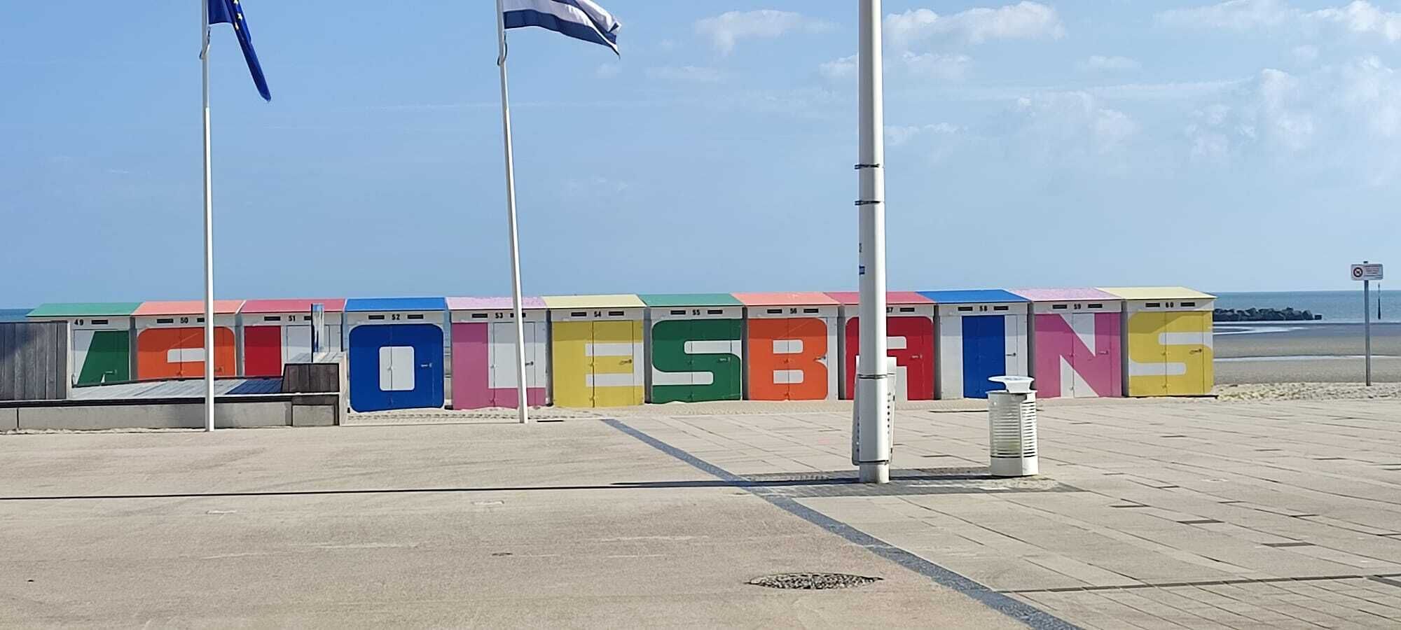 A beachside promenade with colorful lockers numbered 49 to 57, a clear sky, and a calm sea in the background.