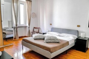Un dormitorio con cama, una silla, una mesita de noche y una ventana con cortinas.