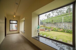 A hallway with a large window overlooking a garden with a stone wall and greenery. - Sri Vidhya Residency (Kotagiri)