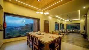 A spacious living room with a large dining table set for a meal, a sofa, and a TV mounted on the wall. - Sri Vidhya Residency (Kotagiri)