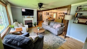 A cozy living room with a fireplace, a sofa, a coffee table, and a television. - Charming 1940s Cottage 
Updated-Creek Front-Fire Pit (Bakersville)