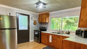 A kitchen with wooden cabinets, a stainless steel refrigerator, a microwave, a stove, and a sink. - Charming 1940s Cottage 
Updated-Creek Front-Fire Pit (Bakersville)