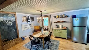 A cozy kitchen with a wooden table, chairs, a chandelier, and a refrigerator. - Charming 1940s Cottage 
Updated-Creek Front-Fire Pit (Bakersville)