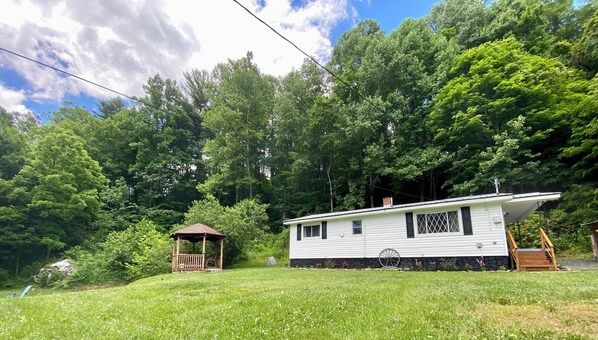 A single-story house with a porch, surrounded by a lush green landscape and dense trees.