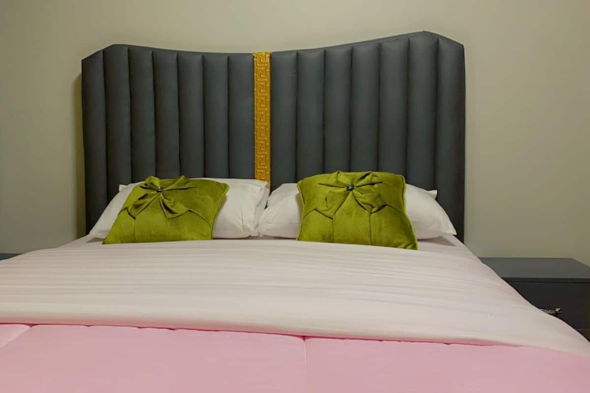 Un lit avec une tête de lit rembourrée de couleur grise, deux coussins verts et un couvre-lit blanc.