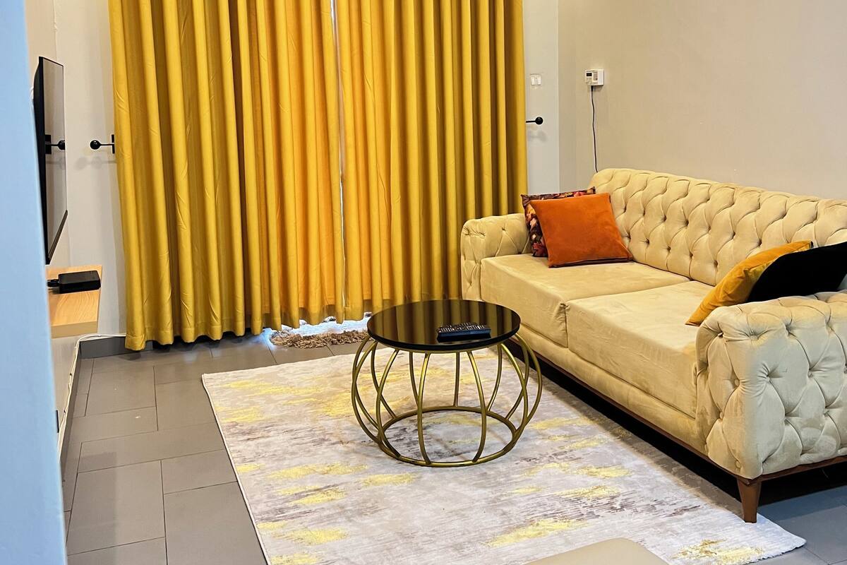 Un salon moderne avec un canapé, une table basse et une grande fenêtre ornée de rideaux jaunes.