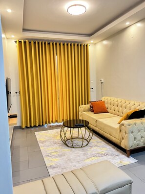 A modern living room with a sofa, a coffee table, and a large window with yellow curtains. - Lee Urban Homes (Kampala)