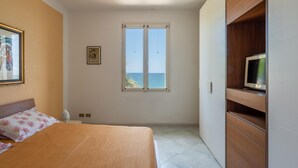 A bedroom with a bed, a television on a wooden cabinet, a window with a view of the sea, and a framed picture on the wall. - Villetta Ficarazzi in Ficarazzi (Ficarazzi)