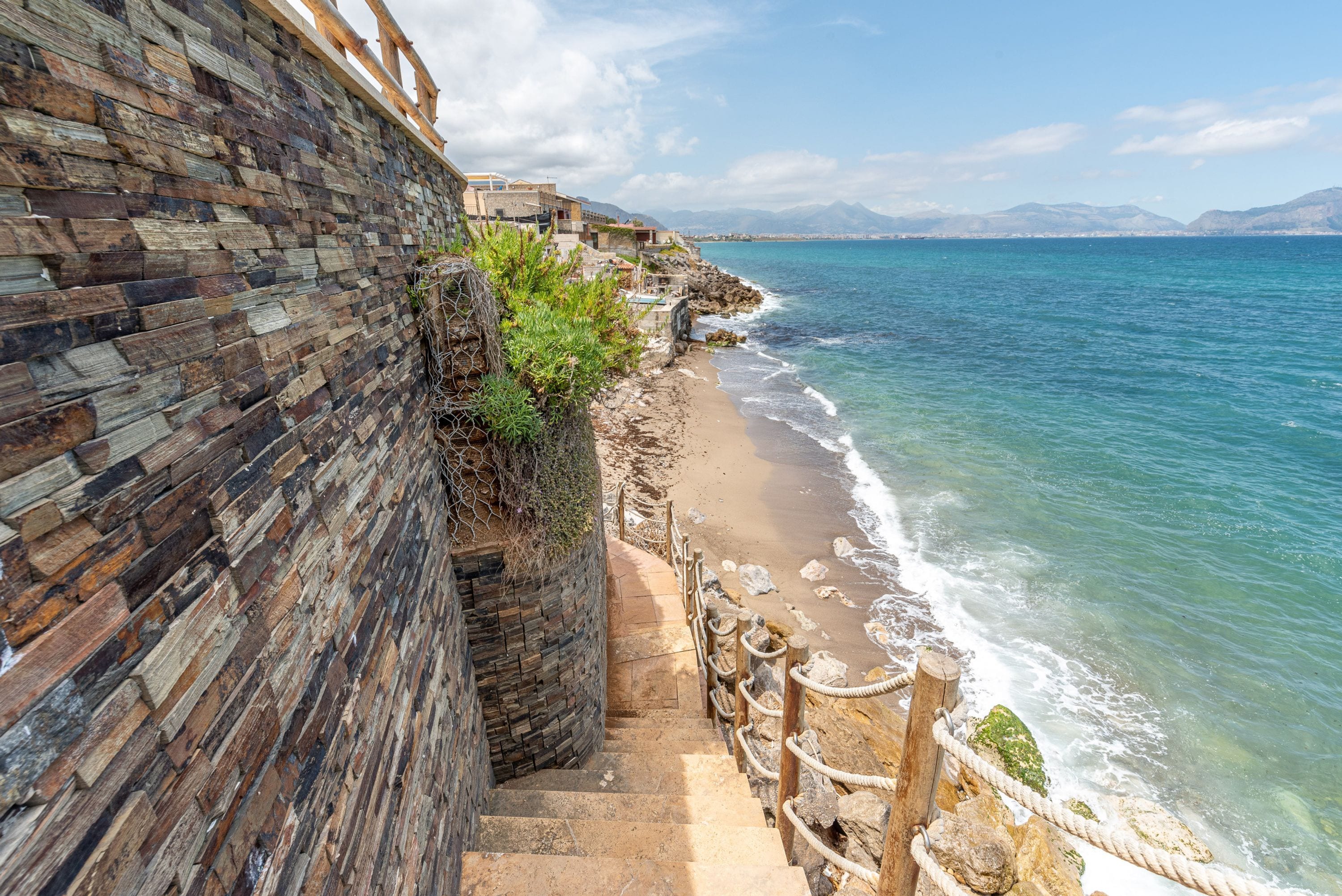 Une promenade en bord de mer, avec un muret en pierre et une vue sur la mer.