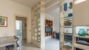 A modern living room with a glass-fronted shelving unit, a dining area with a table and chairs, and a view into another room through an open doorway. - Villetta Ficarazzi in Ficarazzi (Ficarazzi)