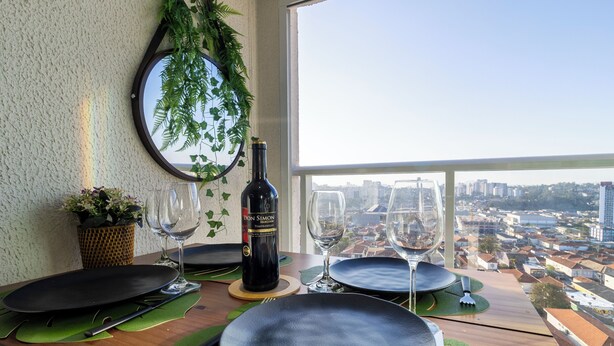 A dining table set with plates, cutlery, and wine glasses, with a bottle of wine and a potted plant on the table. - Piscina academia metro  Brazilian Corner (São Paulo)