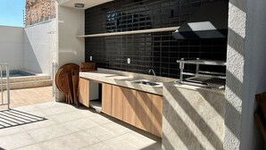 A modern outdoor kitchen with a black tiled backsplash, wooden cabinets, and a built-in grill. - Piscina academia metro  Brazilian Corner (São Paulo)