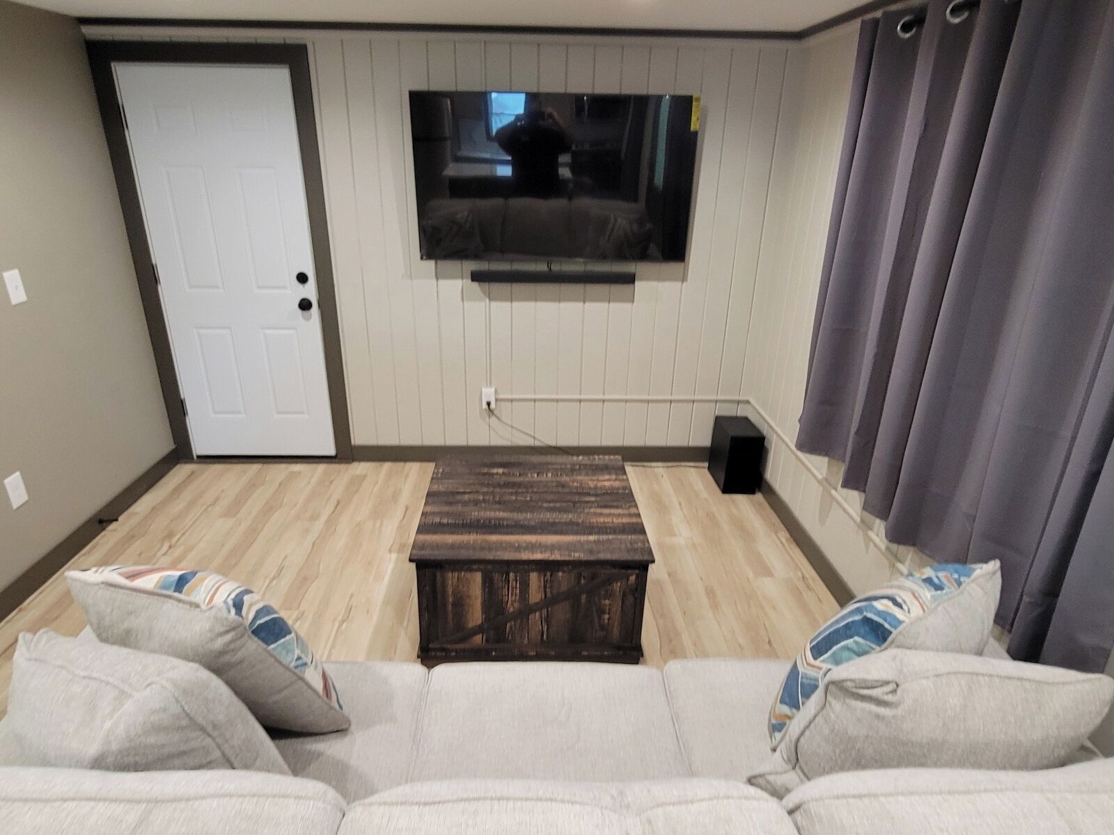 A living room with a sofa, a coffee table, a TV mounted on the wall, and a door.