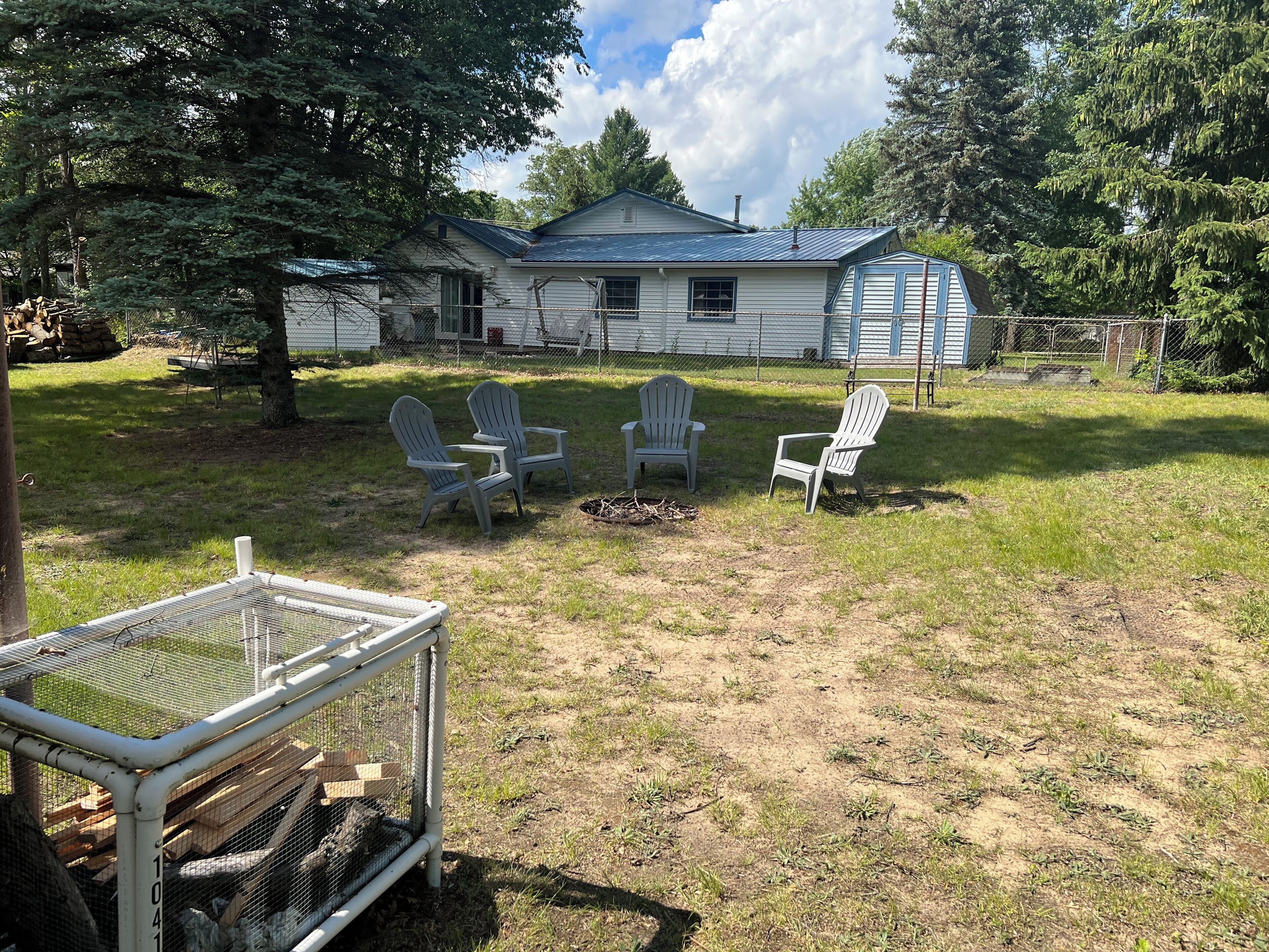 A house with a fenced yard, three Adirondack chairs, and a birdcage.