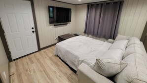 Ein Schlafzimmer mit Bett, einem an der Wand montierten Fernseher und einem Fenster mit Vorhängen.