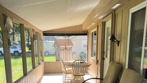 Eine überdachte Veranda mit Tisch und Stühlen, Blick auf einen Garten und ein Holzzaun.
