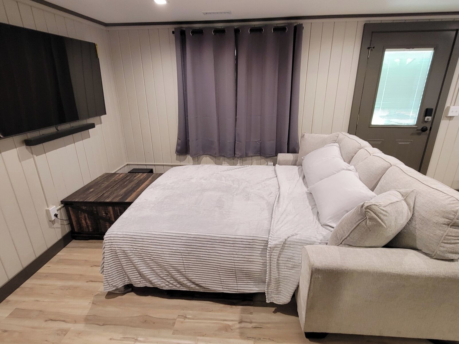 Une chambre à coucher comprenant un lit, un canapé, un téléviseur fixé au mur et une porte avec une fenêtre.