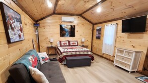 Ett mysigt rum med träpanel på väggarna, en soffa, en säng med festliga sängkläder, ett litet bord och en tv som är monterad på väggen.