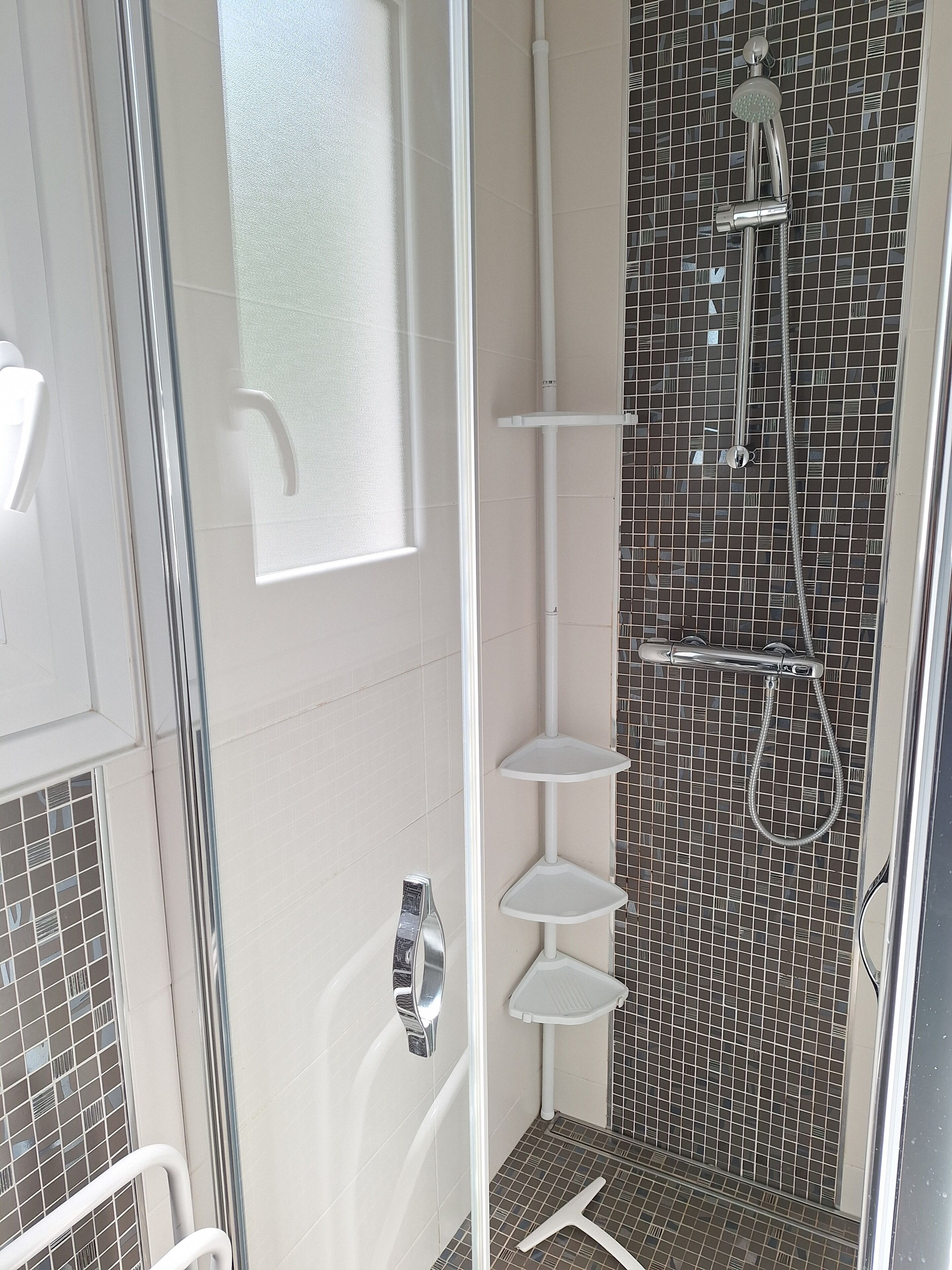 Een moderne badkamer met een glazen douchecabine, witte betegelde wanden en een zwart-wit mozaïek betegelde douchehoek.