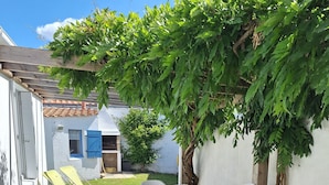 Un patio con una mesa y sillas, una silla lounge amarilla y una pared blanca.