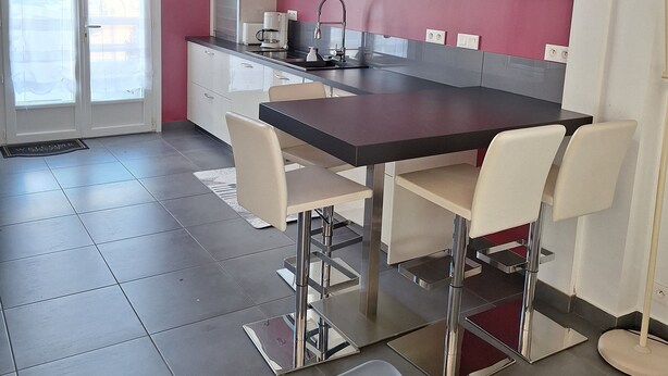 Una cocina moderna con comedor, que incluye una mesa grande y sillas, una cafetera y vistas a través de la puerta de cristal.