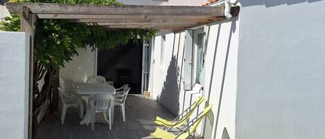 A covered patio with a table and chairs, a small window, and a grassy area.