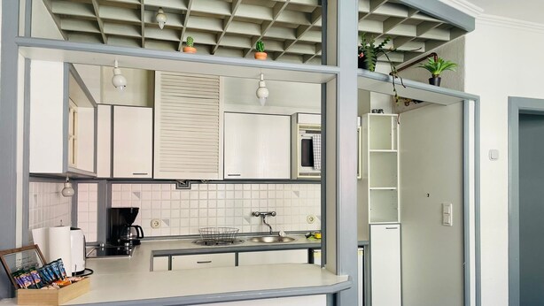 A modern kitchen with white cabinets, a built-in microwave, and a small island with a sink. - Quartier 2 - Ferienwohnung Zentral Gelegen (Bremerhaven)