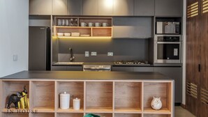 A modern kitchen with built-in appliances, wooden shelves, and a central island. - Luxe & bright ap in poblado /AC - Morph1401 (Medellín)