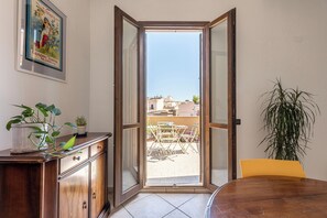 A room with a wooden cabinet, a dining table, and a chair. There is a large window with a view of buildings outside. - The Terrace Behind the Cathedral by Wonderful Italy (Palermo)