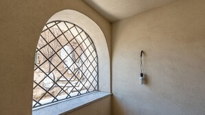Een kamer met een raam met metalen spijlen, een lichtschakelaar aan de muur en uitzicht op een buitenruimte met een standbeeld.