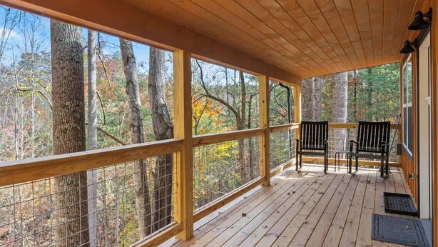 A wooden deck with a railing, two black chairs, and a view of trees. - Cozy Couples Cabin in Heart of RRG! (Campton)