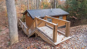 A cabin with a metal roof, wooden deck, and a staircase leading to a wooden platform. - Cozy Couples Cabin in Heart of RRG! (Campton)