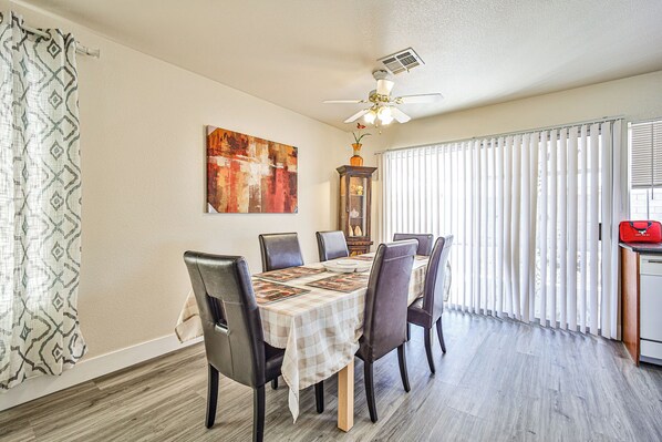 A dining area with a table set for four, a ceiling fan, a cabinet with decorative items, and a window with blinds.