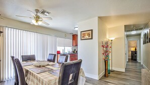 Un coin repas avec une table dressée pour quatre personnes, un ventilateur de plafond et une cuisine en arrière-plan.