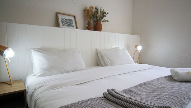 Een net opgemaakt bed met witte lakens, twee bedlampen en een deken met een patroon.