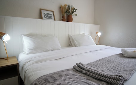 A neatly made bed with white linens, two bedside lamps, and a patterned throw blanket.