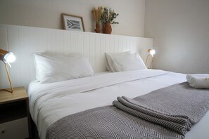 A neatly made bed with white linens, two bedside lamps, and a patterned throw blanket. - CURIOCITY Kloof Street (Cape Town)