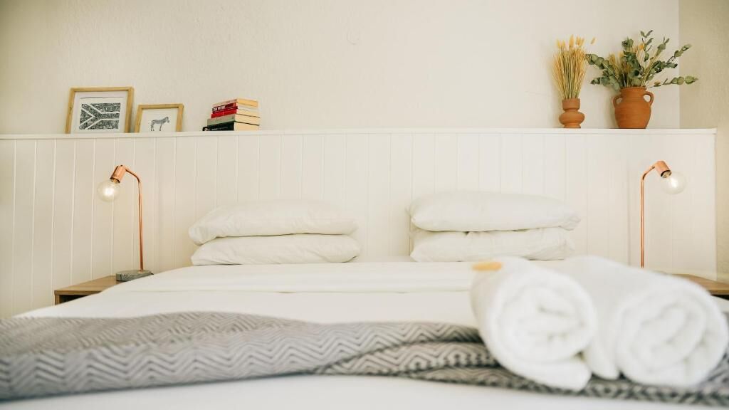 A neatly made bed with white linens, two bedside lamps, and a bedside table with a book and a framed picture.