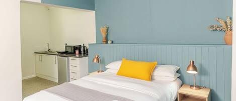 A bedroom with a bed, bedside tables, a ceiling fan, and a kitchenette in the adjacent room.
