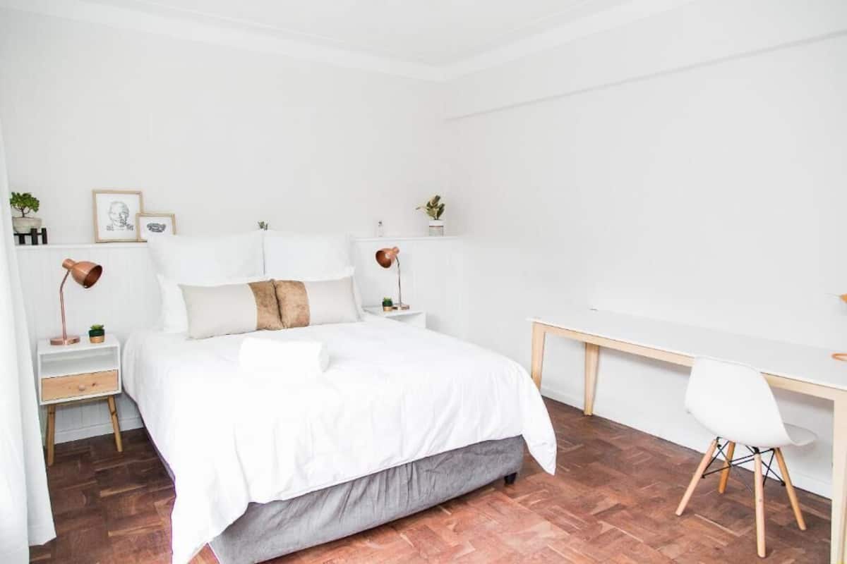 Une chambre à coucher au style minimaliste, avec un lit, des tables de chevet, un bureau et une chaise.