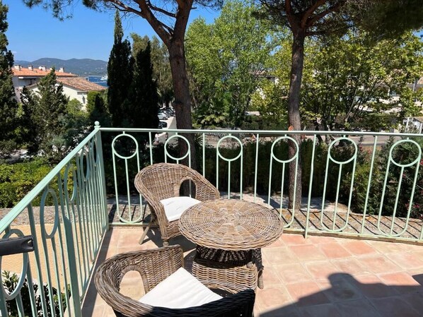 Un balcon doté de meubles en osier, d’une rambarde en métal et offrant une vue sur la mer et les bâtiments qui se dressent à l’arrière-plan.