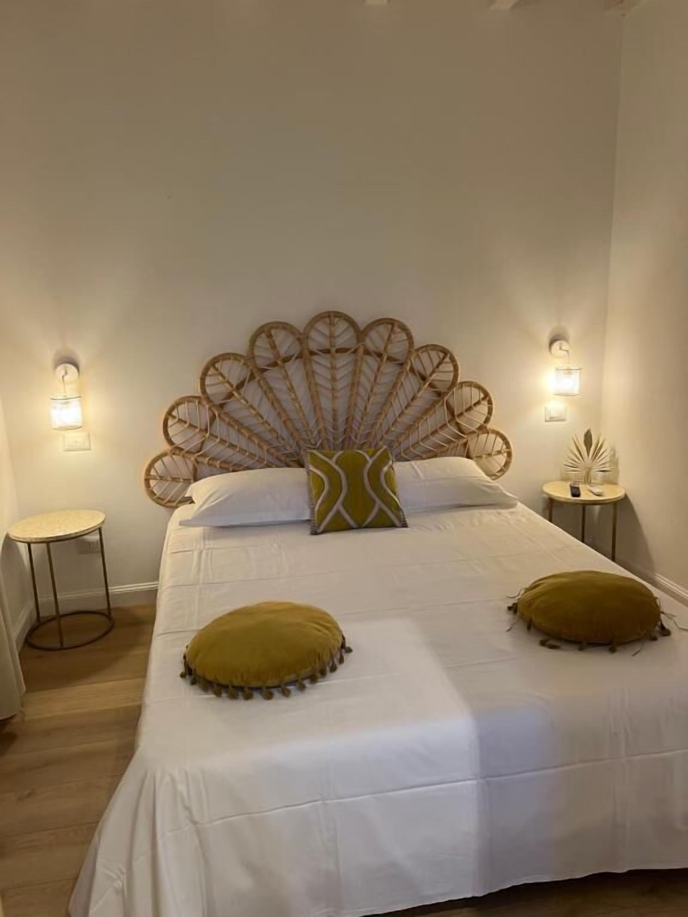 A neatly made bed with a decorative headboard, two bedside tables, and a wall-mounted light fixture.