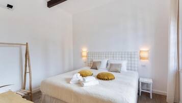 A bedroom with a large bed, two bedside lamps, a small bedside table, and a wooden ladder against the wall.