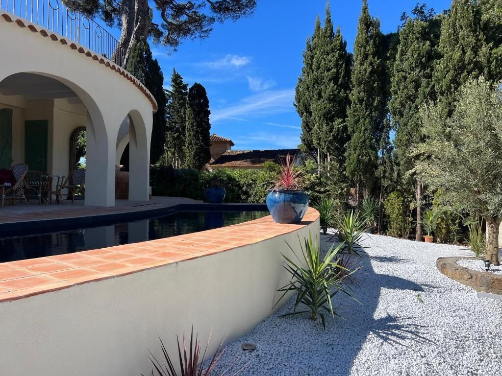 A pool area with a tiled deck, a pergola, and a variety of plants.