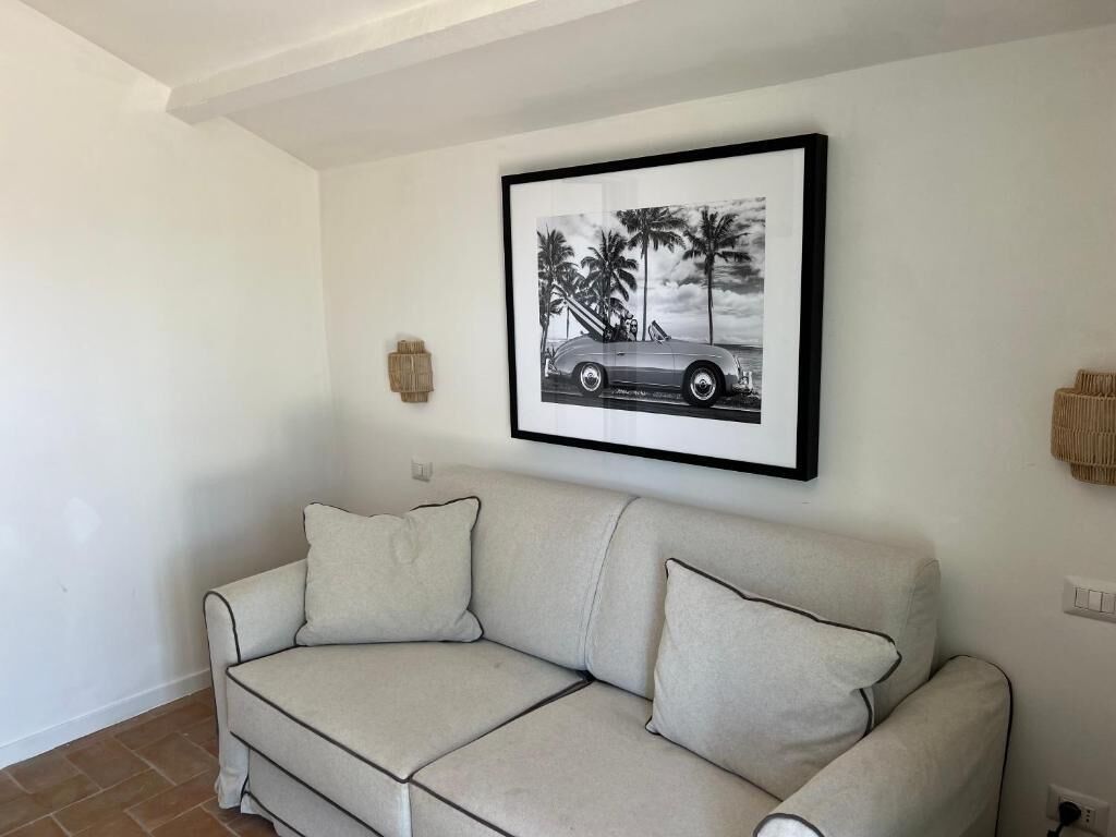 A living room with a beige sectional sofa, a framed black and white car picture, and a small wall-mounted light fixture.