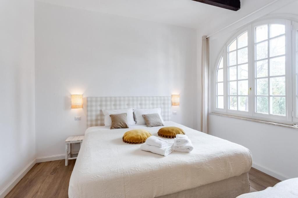 Une chambre avec un grand lit, deux tables de chevet, une fenêtre aux cadres blancs et une tête de lit à carreaux.